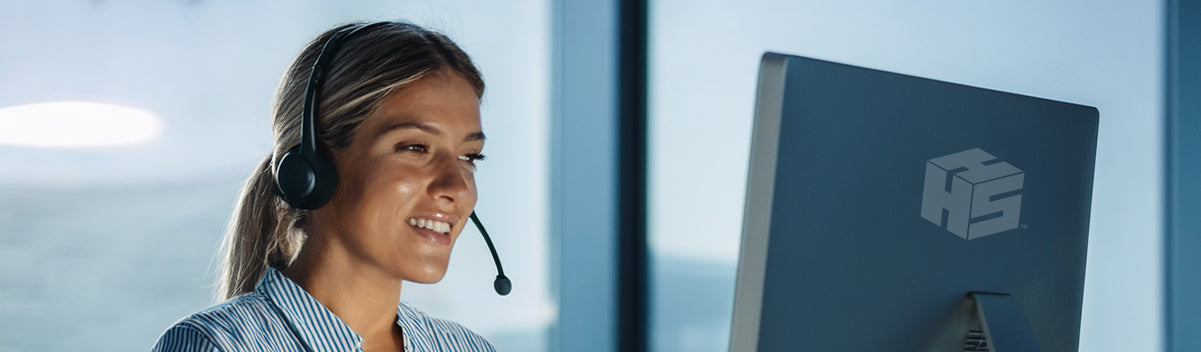 Female wearing a headset in front of a computer screen with a Hang It Simple cube logo, in an office setting.