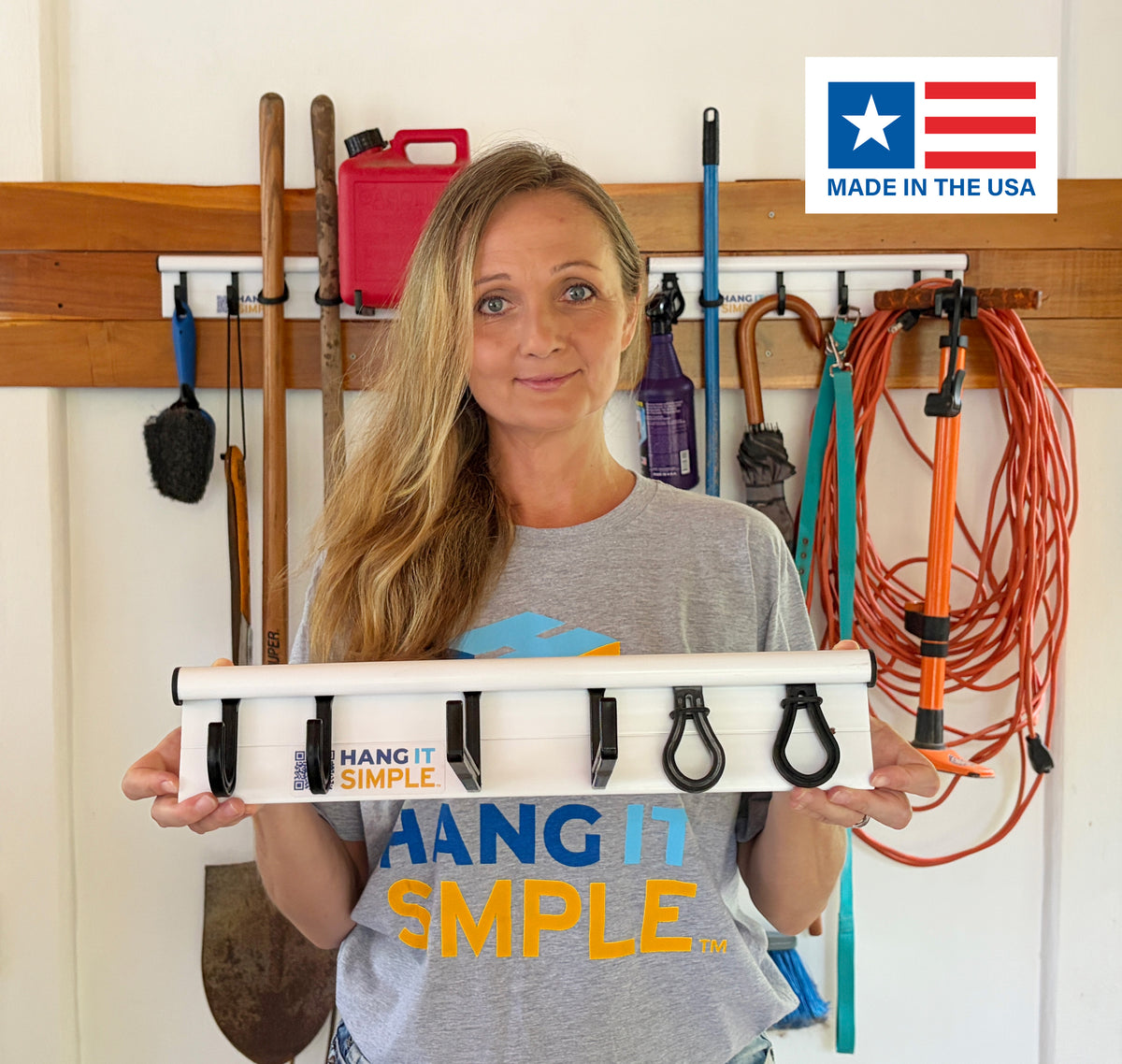Woman holding a 'Hang It Simple' product in front of a wall with various tools and equipment.