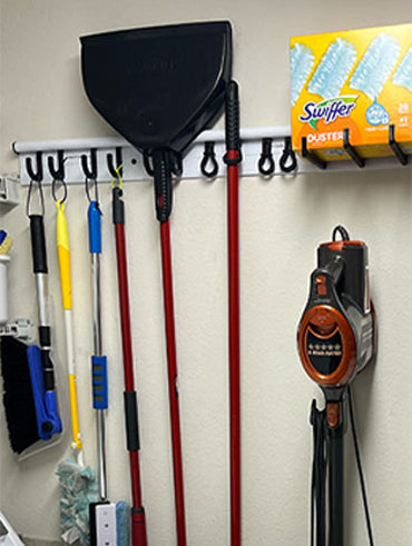 Wall mounted Hang It Simple 36" starter kit with brooms, mops, and dust pans hanging on it. 