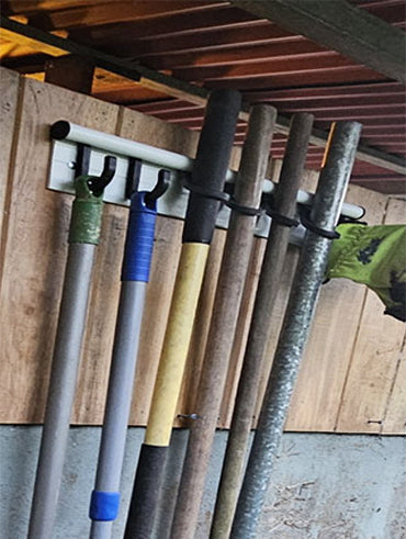 Set of gardening tools hanging on Hang It Simple 18" starter kit rail on a wooden wall.